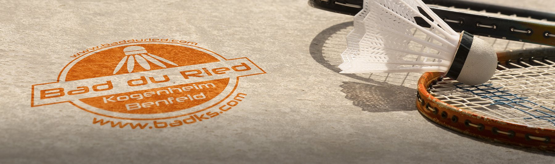 Image large incluant un sol avec le logo Bad du Ried en marquage au sol, une raquette au sol et un volant